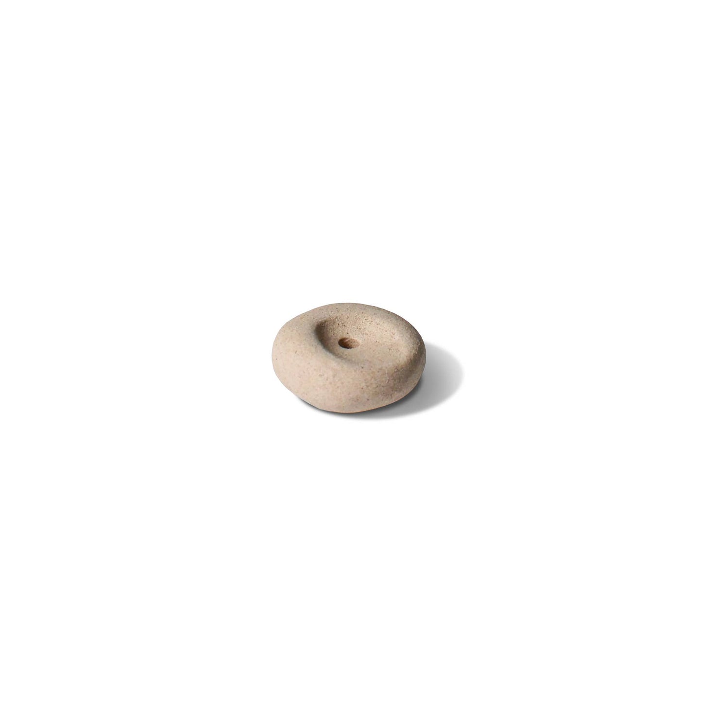 Clay pebble incense holder in soft beige tones, shown on a pale fabric background with a raw, organic finish.