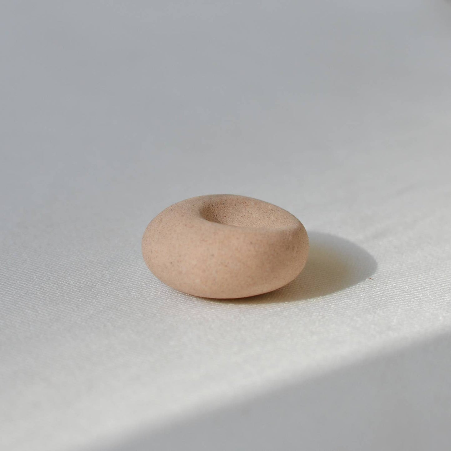 Clay pebble incense holder in soft beige tones, shown on a pale fabric background with a raw, organic finish.