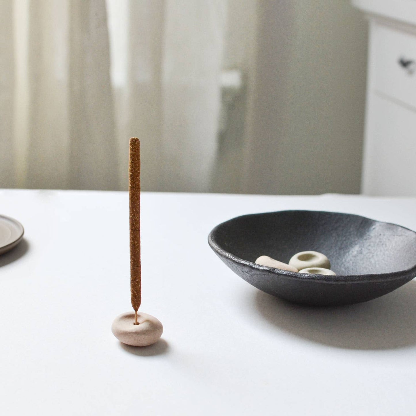 Clay incense holder displayed beside a black ceramic bowl on a neutral background, highlighting its natural texture.