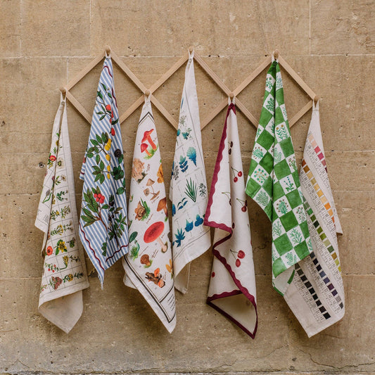 Array of vintage-style print tea towels hanging against a rustic stone wooden backdrop.