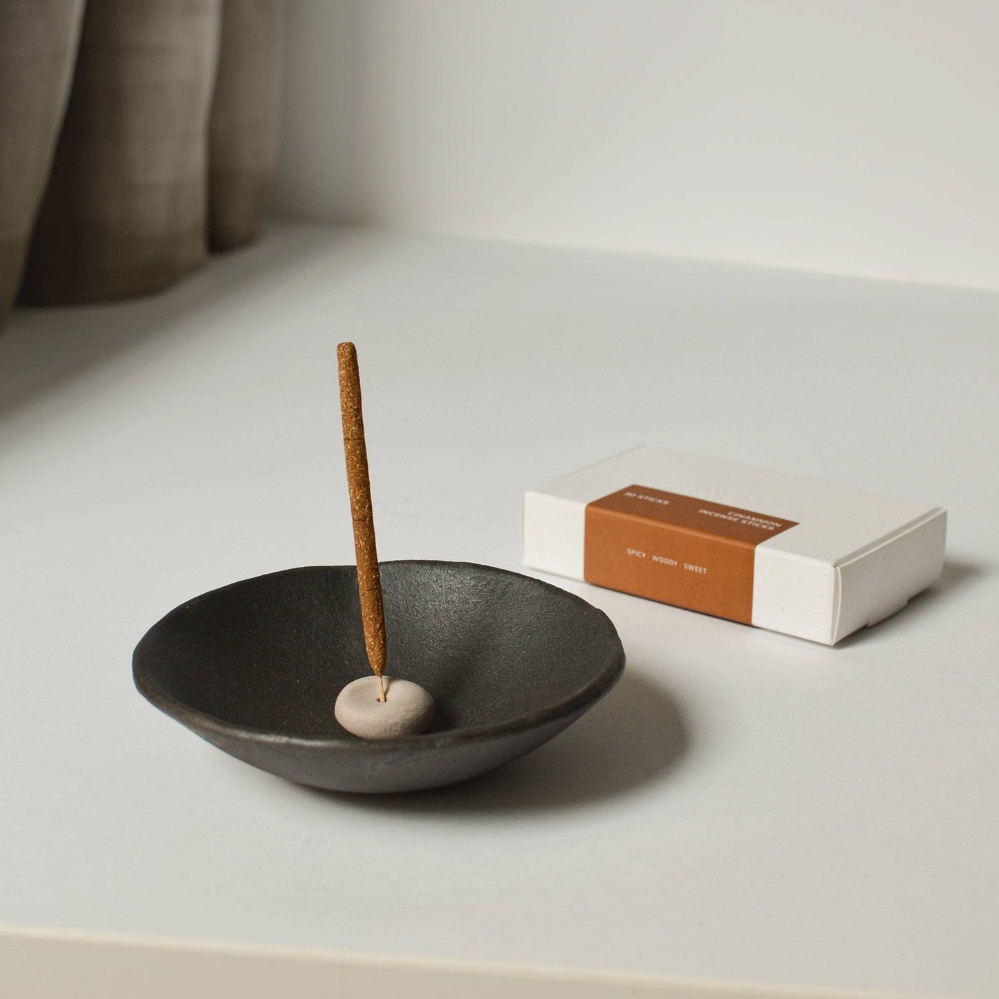 Handcrafted beige clay incense holder placed inside a larger black dish, styled with incense sticks beside it.