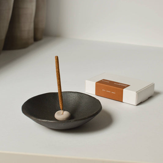 Handcrafted beige clay incense holder placed inside a larger black dish, styled with incense sticks beside it.