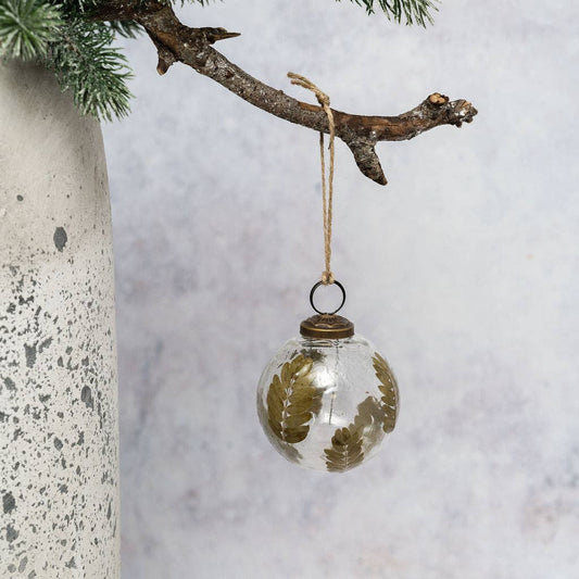 Clear mouth-blown Christmas bauble holding fine stems and leaves