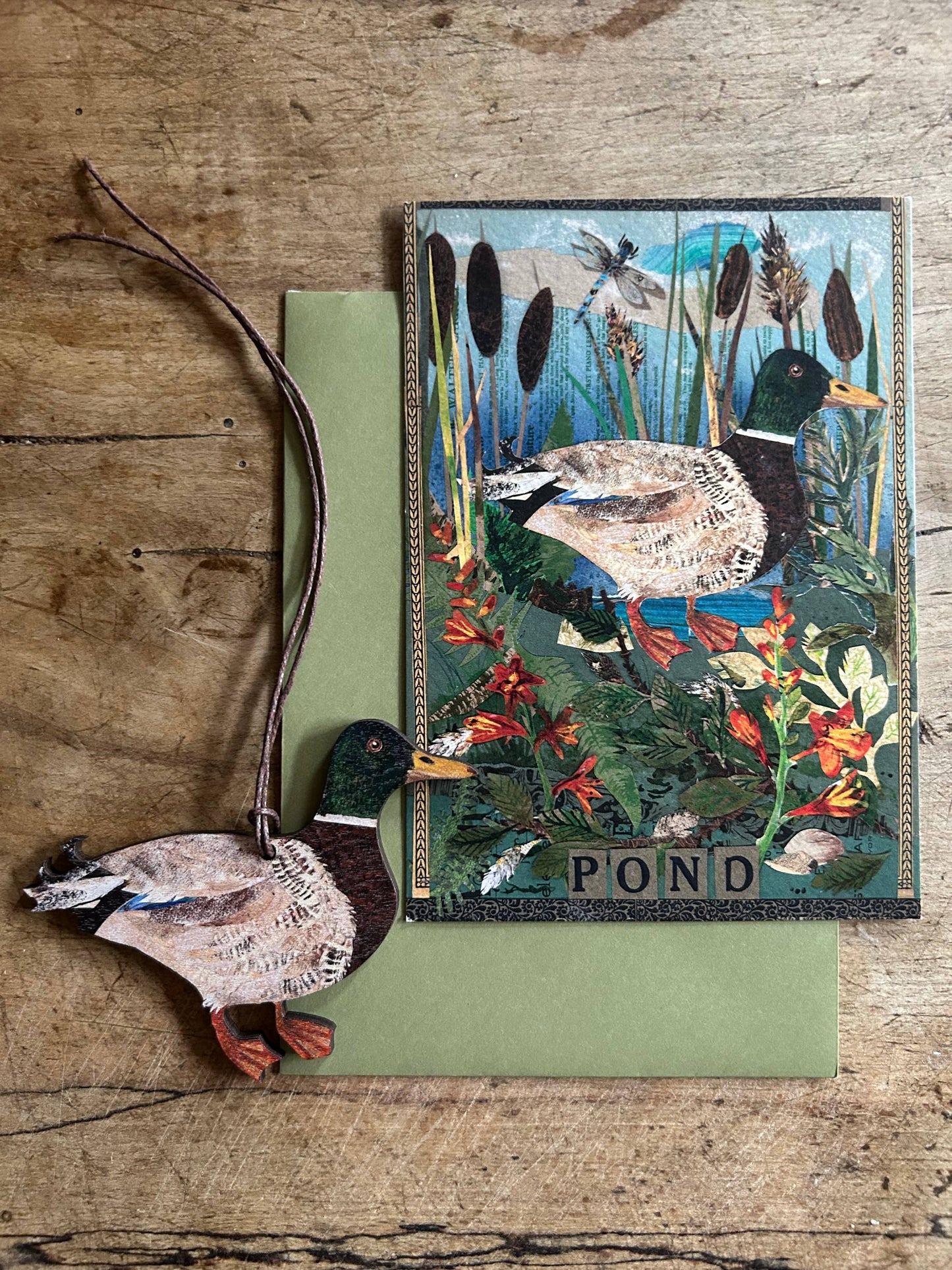 Decorative card with a duck design and 'Pond' text, accompanied by a wooden duck on a wooden surface.