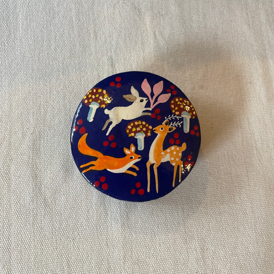 Hand-painted blue papier-mâché trinket box with woodland design on plain linen backdrop