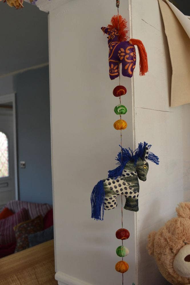 Decorative hanging mobile with colorful beads and animal figures on a white wall.