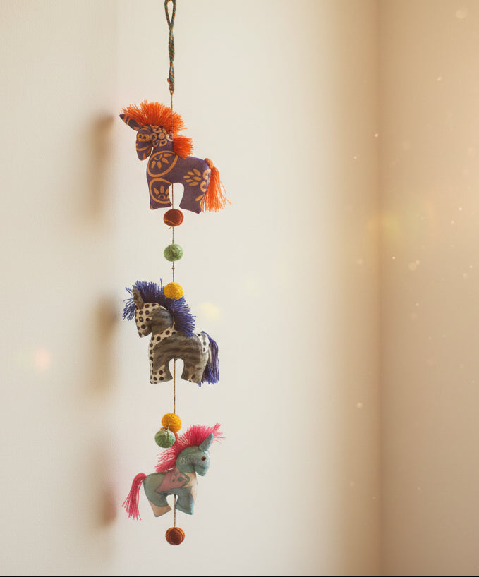 Colorful horse-shaped toy mobile hanging from a vertical string on a white background
