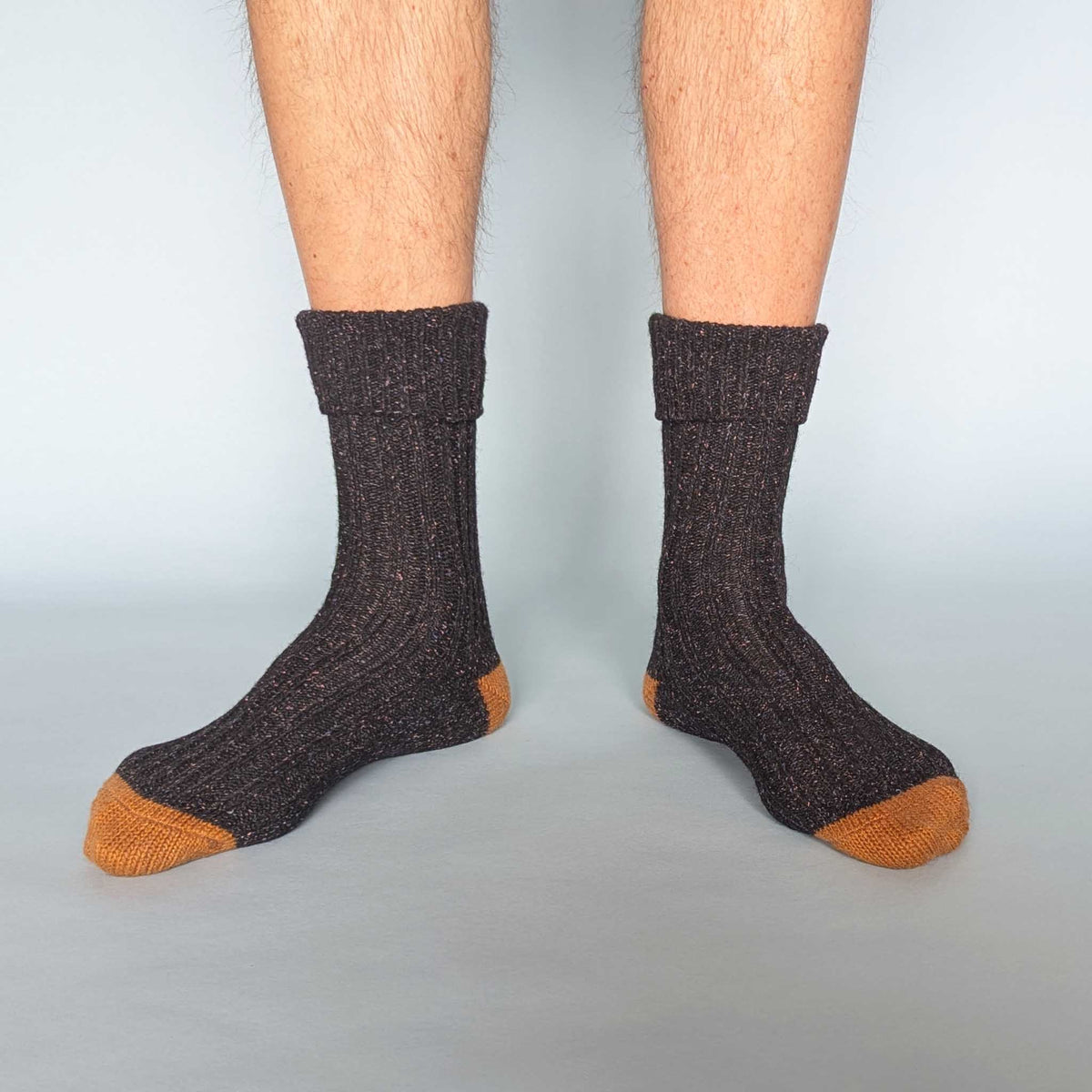 Dark brown socks with orange toes and cuffs worn by a person on a light blue background