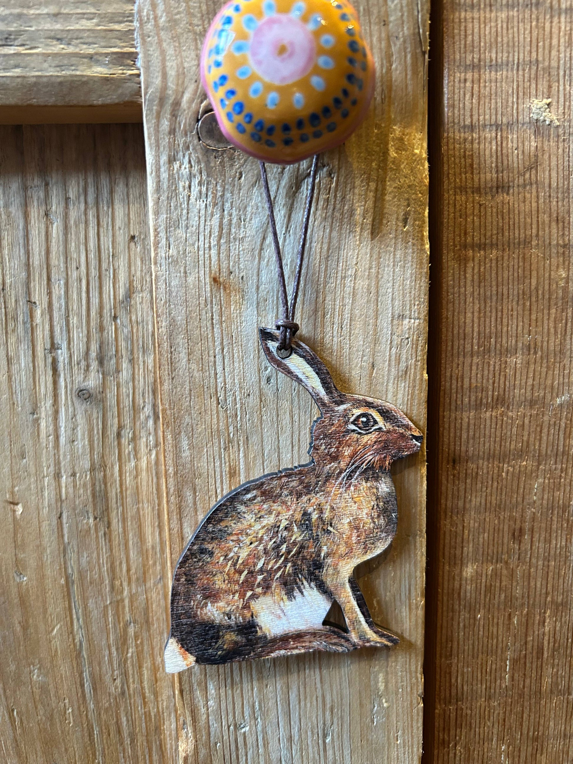 Decorative rabbit charm hanging from a colourful ceramic doorknob on a wooden background