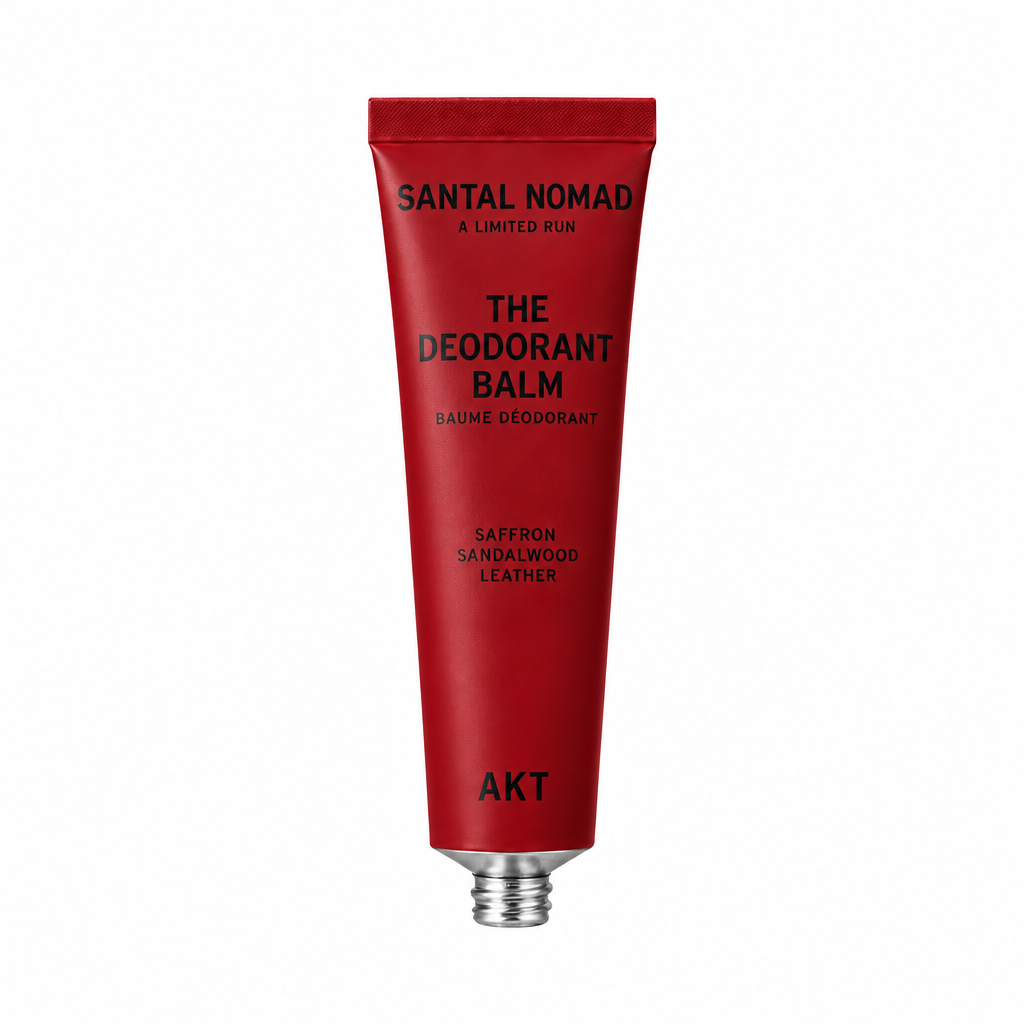 A red squeeze tube of Santal Nomad The Deodorant Balm on a transparent checkerboard background, labeled Saffron Sandalwood Leather.