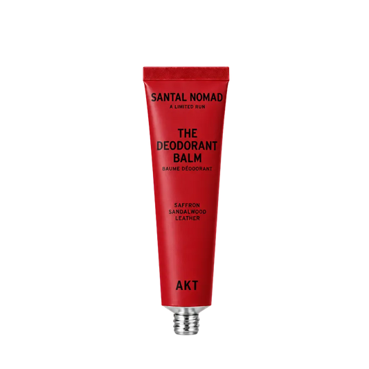 A red squeeze tube of Santal Nomad The Deodorant Balm by AKT, featuring black text and a silver metal cap, centered on a plain white background.