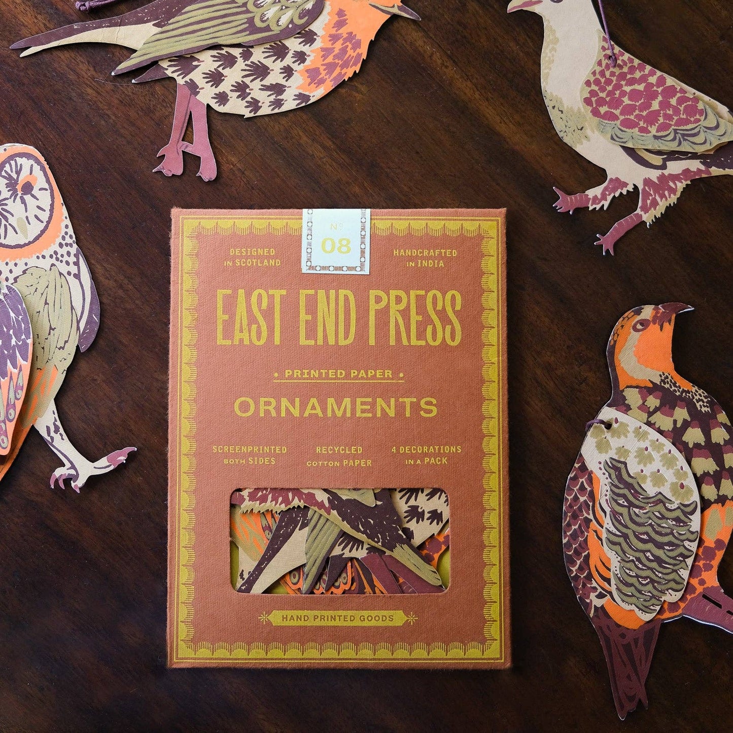 Box of East End Press ornaments with decorative paper birds on a wooden surface