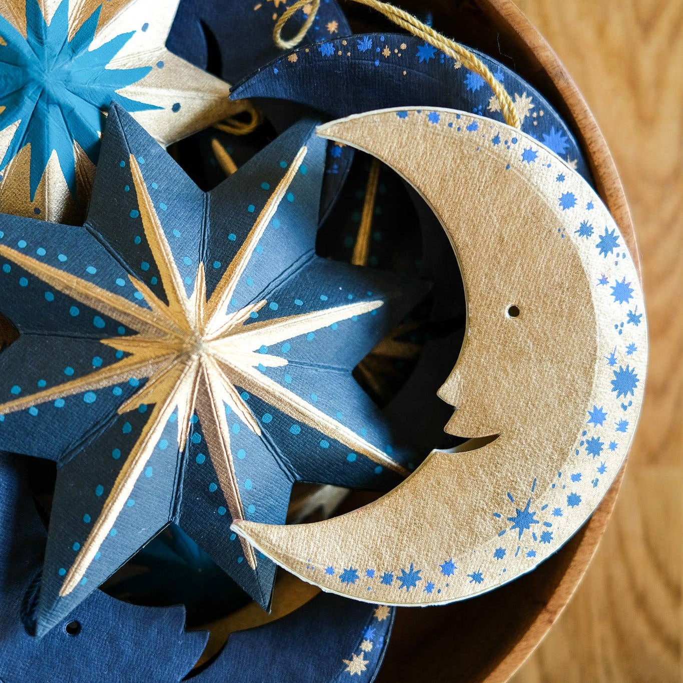 Decorative paper stars and moon with starry patterns in a box on a wooden surface