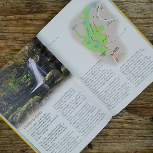 Open book with a map and photograph of a waterfall and a trail map on a wooden surface