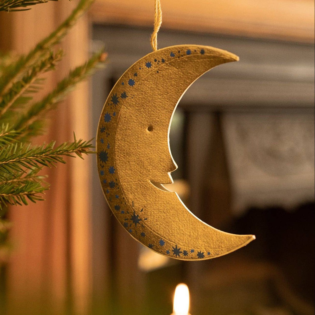 Decorative paper moon-shaped ornament with star patterns hanging on a tree.