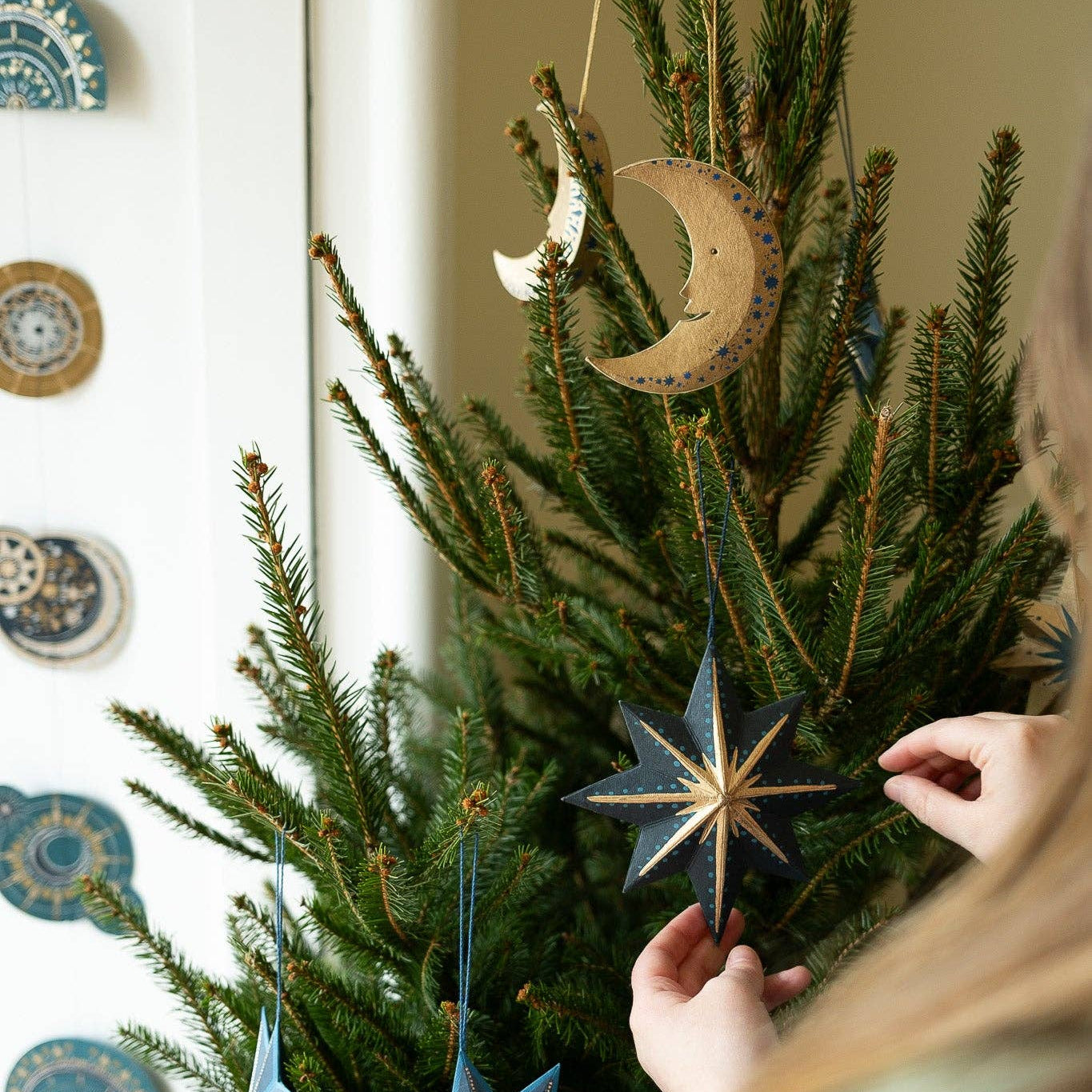 Person decorating a Christmas tree with star-shaped ornaments in a home setting.