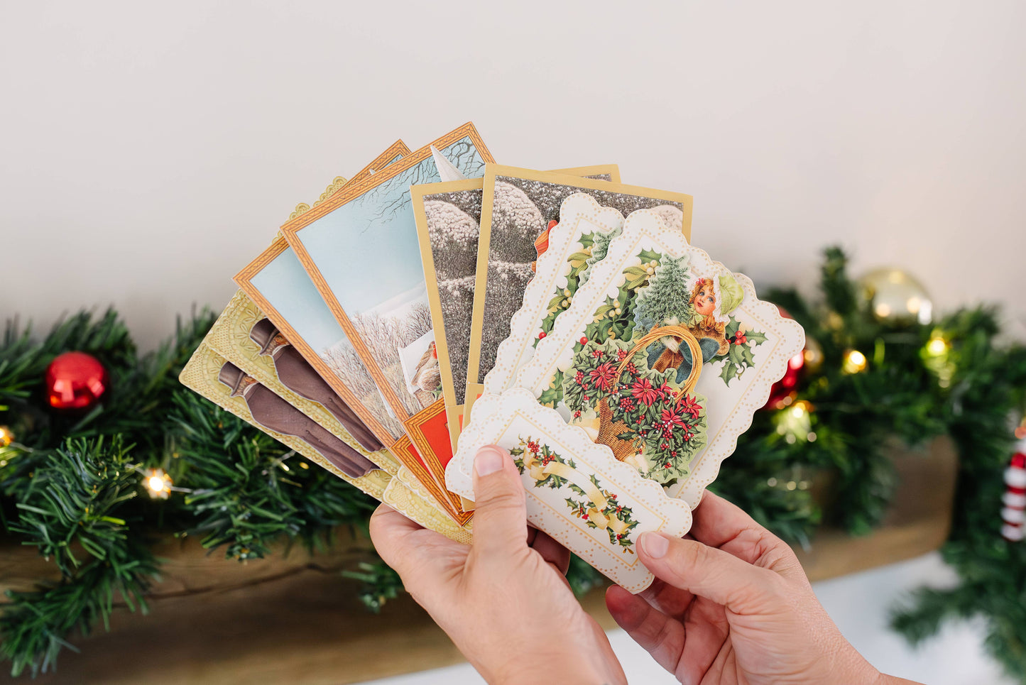 Hand holding victorian style Christmas cards with festive decorations in the background