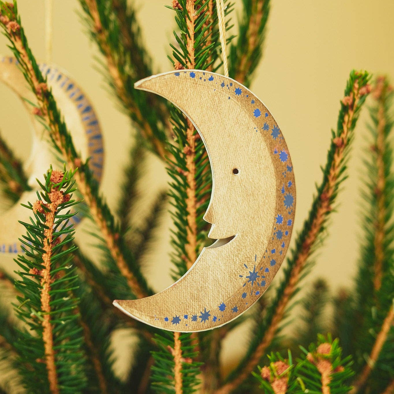 Decorative moon-shaped ornament with a face on a Christmas tree branch