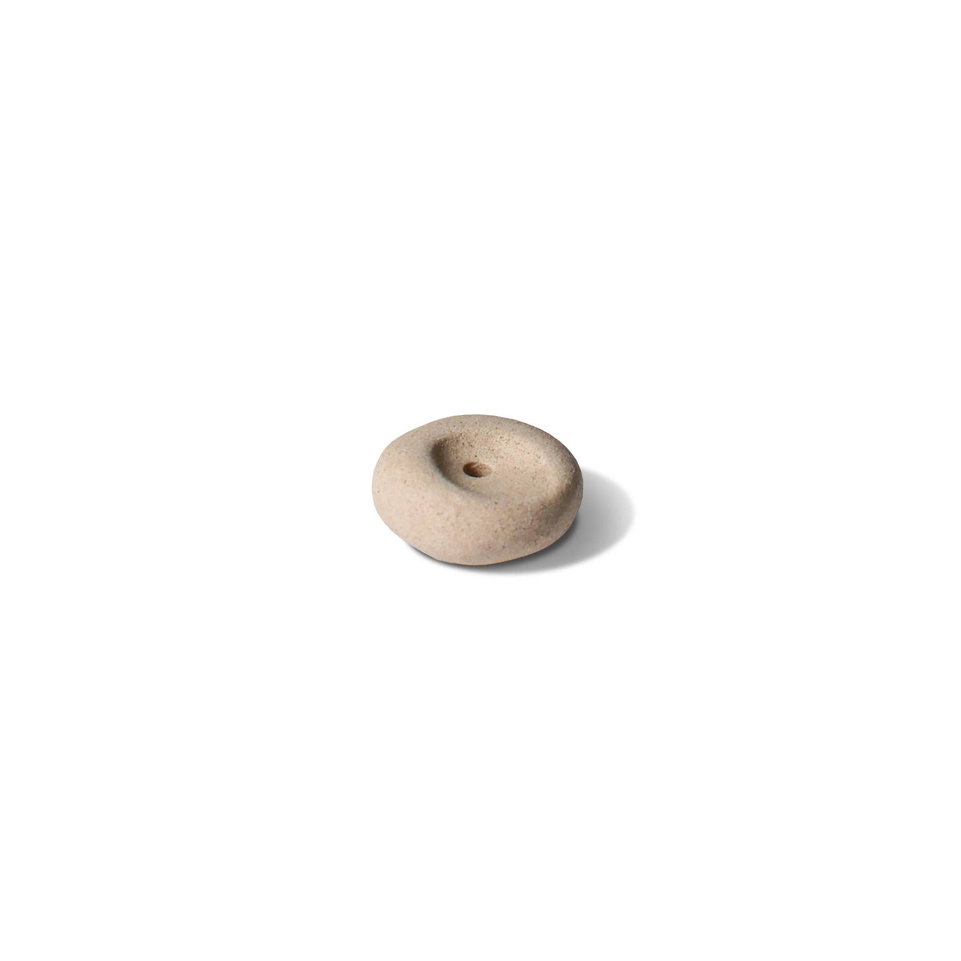 Clay pebble incense holder in soft beige tones, shown on a pale fabric background with a raw, organic finish.