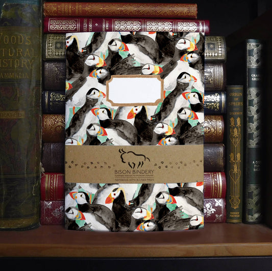 Notebook with puffin design on a stack of antique books with Bison Bindery branding