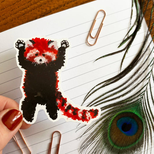 Sticker of a red panda on lined paper with a peacock feather and paperclip.
