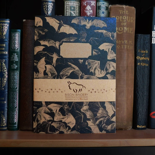 hand-painted bat notebook with Bison Bindery branding on a shelf with antique books 