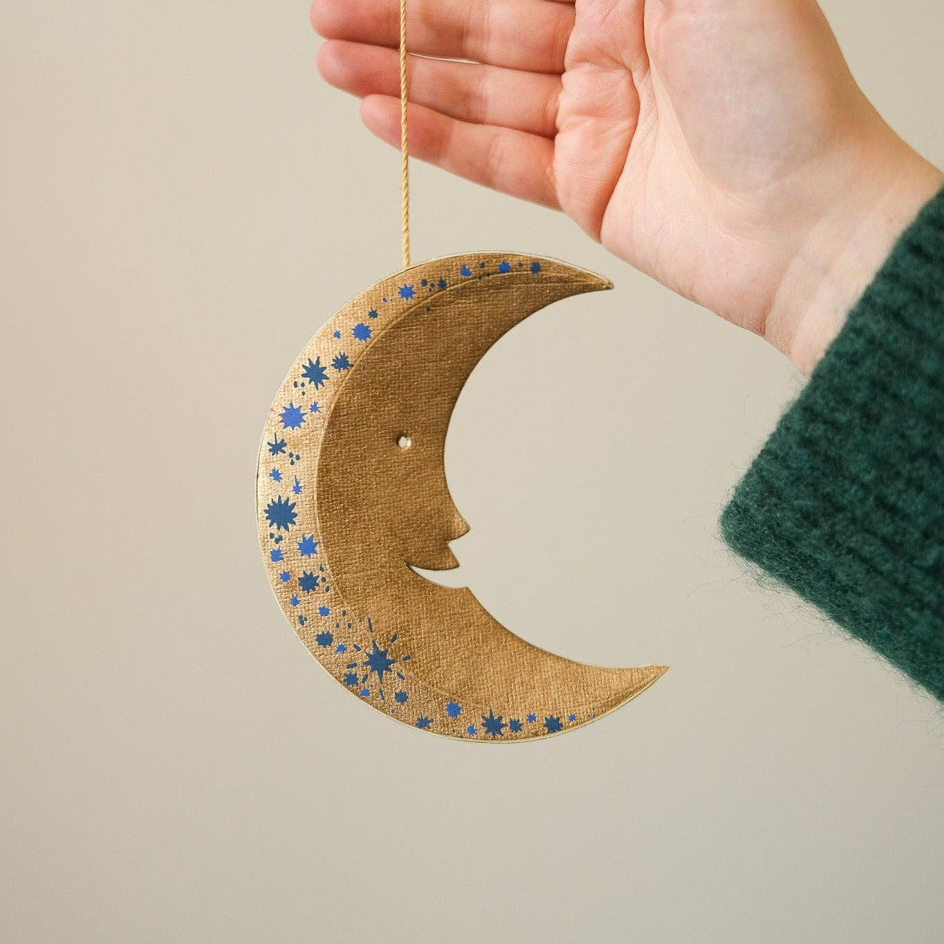 Hand holding a decorative moon-shaped ornament with star patterns against a neutral background