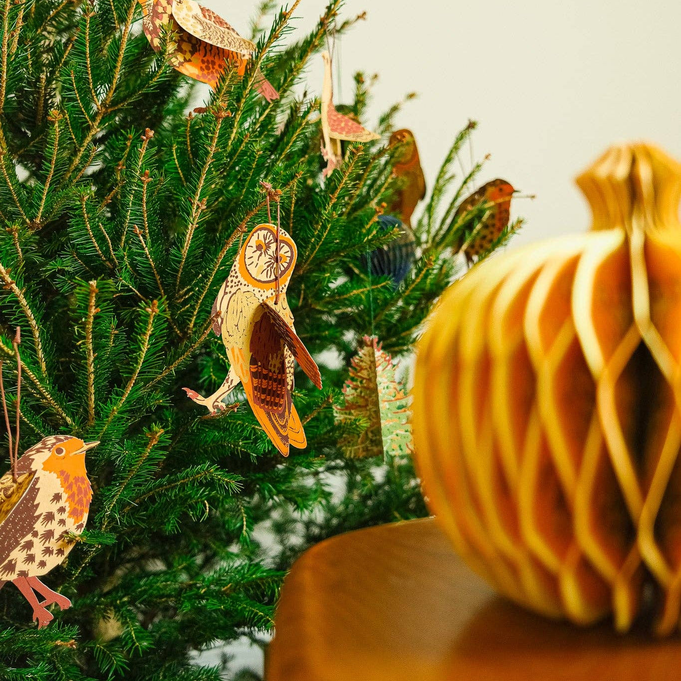 Decorative Christmas tree with  paper bird ornaments and a pumpkin on a table.