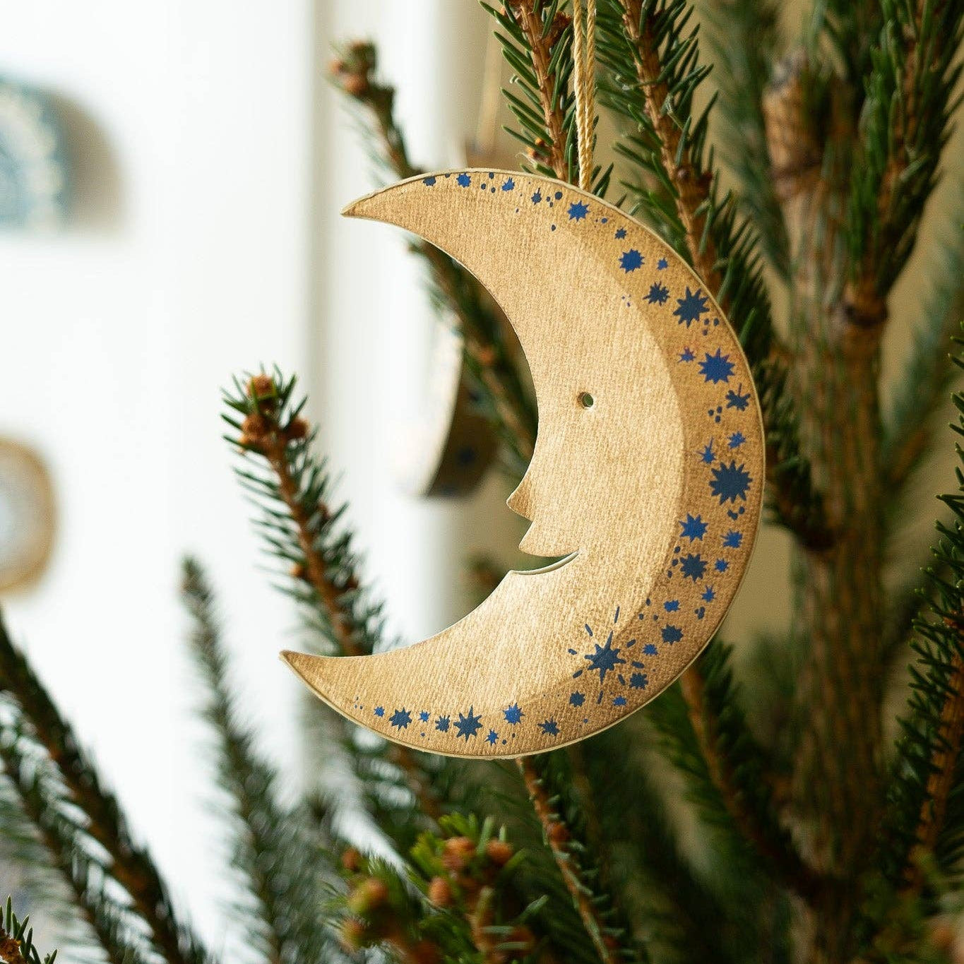 recycled paper, moon-shaped ornament with star patterns hanging on a Christmas tree.