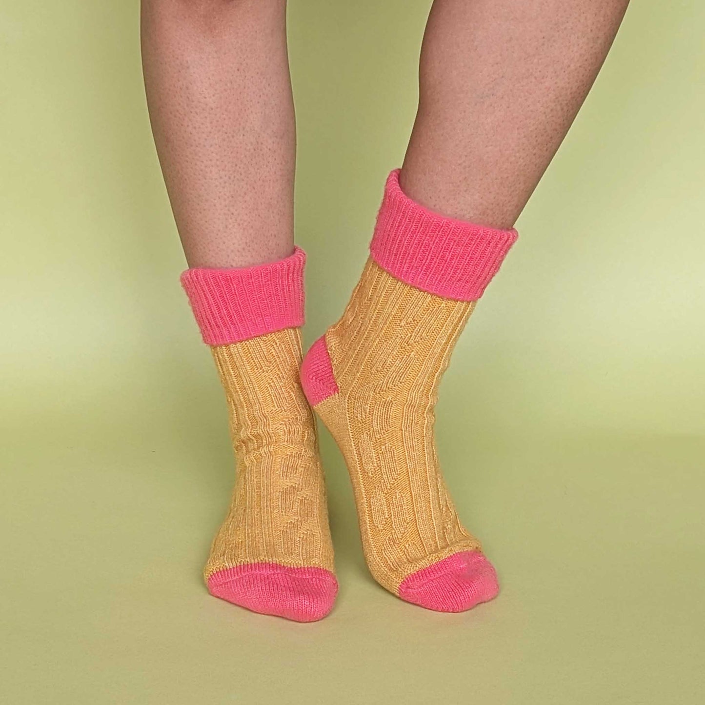 Yellow slouch socks with coral pink cuffs and toes on a green background