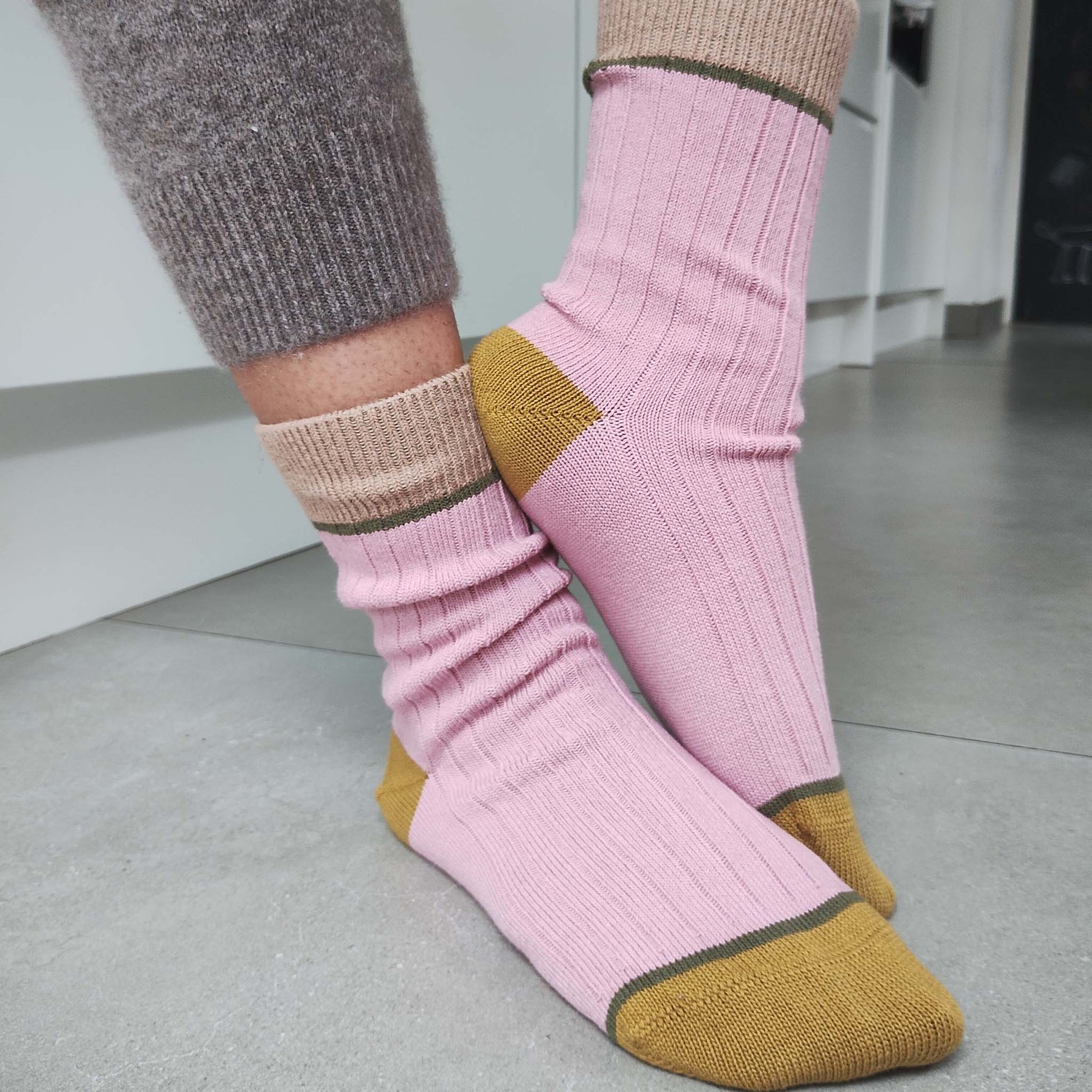 Pink and mustard yellow socks worn with gray wool leggings on a neutral background