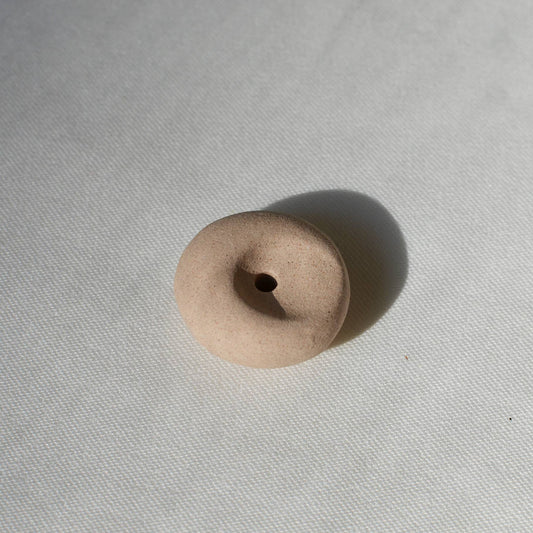 Clay pebble incense holder in soft beige tones, shown on a pale fabric background with a raw, organic finish.