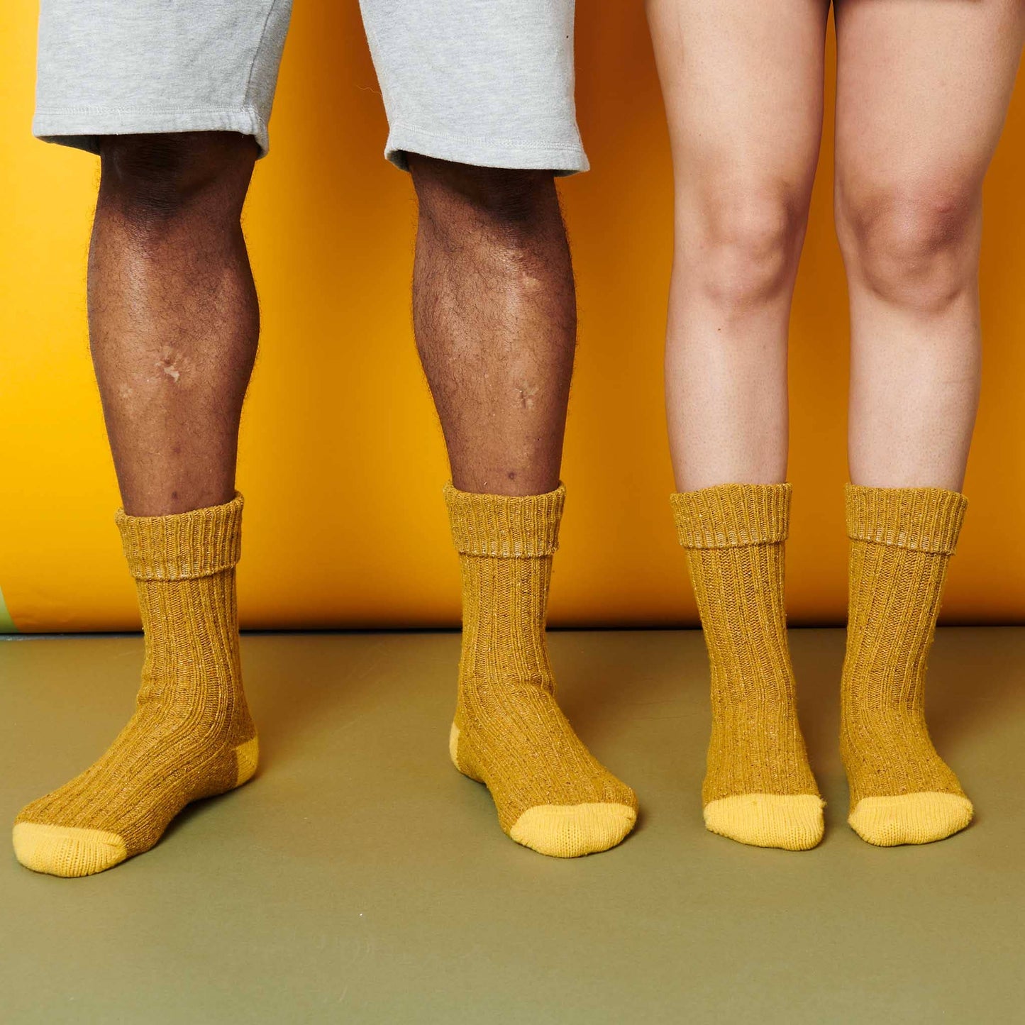 Two pairs of legs wearing mustard yellow socks against a yellow background