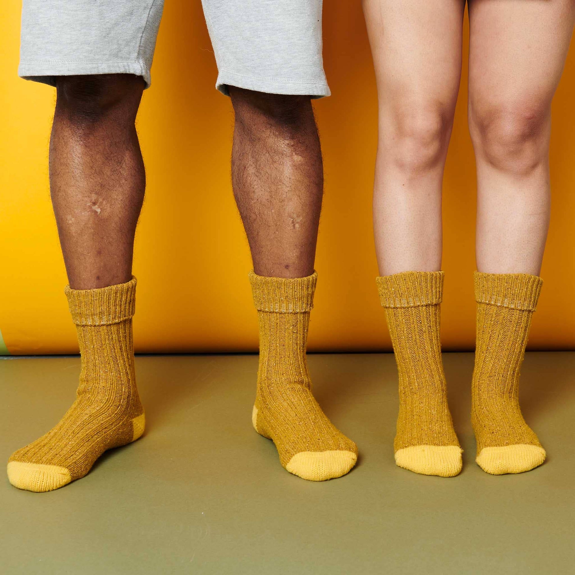 Two pairs of legs wearing mustard yellow socks against a yellow background